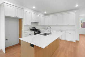 Kitchen featuring an island with sink, gas range, white cabinets, and sink