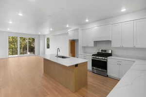 Kitchen featuring stainless steel range, an island with sink, sink, and white cabinetry