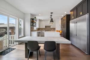 Kitchen with decorative backsplash, hanging light fixtures, white cabinetry, light wood-type flooring, and stainless steel appliances