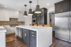 Kitchen featuring dark wood-type flooring, stainless steel appliances, hanging light fixtures, and white cabinets