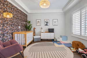 Bedroom featuring a raised ceiling, wood-type flooring, ornamental molding, and a nursery area