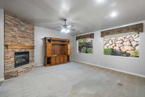 Unfurnished living room featuring a stone fireplace, carpet floors, and ceiling fan