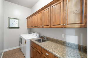 Clothes washing area with sink, light tile patterned floors, cabinets, and separate washer and dryer