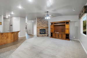 Living room with a fireplace, a textured ceiling, ceiling fan, vaulted ceiling, and light colored carpet