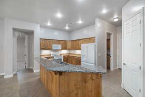 Kitchen with dark stone countertops, light tile patterned flooring, a kitchen bar, a textured ceiling, and white appliances