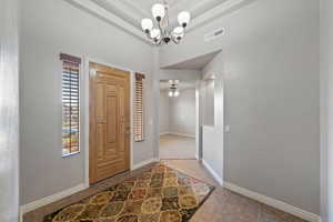 Tiled foyer featuring ceiling fan with notable chandelier