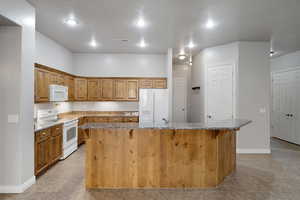 Kitchen with white appliances, light tile patterned floors, a center island, light stone counters, and a breakfast bar