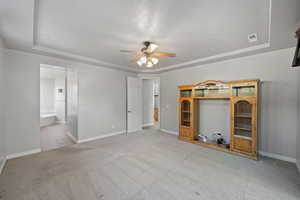 Unfurnished living room with ceiling fan, a raised ceiling, a textured ceiling, and light colored carpet