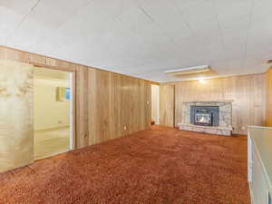 Unfurnished living room with carpet, a stone fireplace, and wood walls