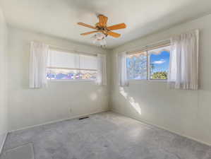 Carpeted spare room featuring plenty of natural light and ceiling fan