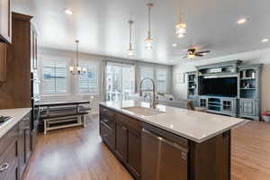 Kitchen with hanging light fixtures, a center island with sink, stainless steel dishwasher, light wood-type flooring, and sink