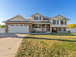 Split level home featuring covered porch, front yard, and garage