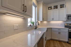 Kitchen featuring appliances with stainless steel finishes, light hardwood / wood-style flooring, white cabinetry, and light stone countertops