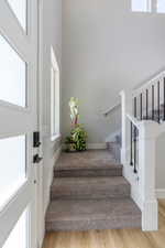 Stairs with a towering ceiling, a healthy amount of sunlight, and hardwood / wood-style flooring