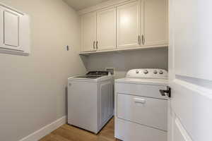 Washroom featuring light wood-type flooring, separate washer and dryer, and cabinets