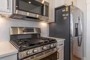 Kitchen with light stone countertops, appliances with stainless steel finishes, backsplash, and white cabinets