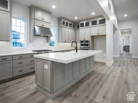 Kitchen with decorative backsplash, a kitchen island with sink, stainless steel appliances, and light wood-type flooring