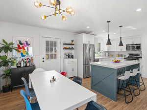 Kitchen with appliances with stainless steel finishes, decorative light fixtures, a kitchen island, and light hardwood / wood-style floors