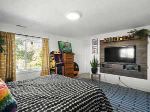 Family room set up as bedroom with a textured ceiling and hardwood / wood-style floors