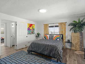 Family room set up as a guest bedroom with a textured ceiling and hardwood / wood-style floors