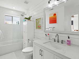 Full bathroom with wood walls, toilet, vanity, tiled shower / bath combo, and tile patterned flooring