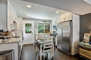 Kitchen featuring appliances with stainless steel finishes, white cabinets, light stone counters, and dark hardwood / wood-style floors