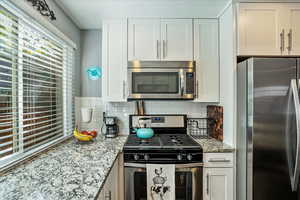 Kitchen featuring appliances with stainless steel finishes, white cabinets, light stone counters, and backsplash