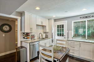 Kitchen featuring white cabinets, stainless steel dishwasher, dark wood-type flooring, sink, and light stone counters