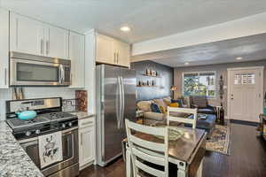 Kitchen with dark wood-type flooring, light stone counters, appliances with stainless steel finishes, and white cabinetry