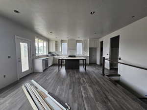 Kitchen with a kitchen island, a textured ceiling, dark hardwood / wood-style flooring, stainless steel dishwasher, and white cabinets