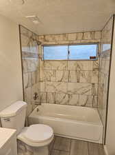 Full bathroom with vanity, tiled shower / bath, a textured ceiling, and toilet