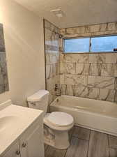 Full bathroom featuring tiled shower / bath, a textured ceiling, a wealth of natural light, toilet, and vanity