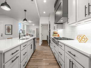 Kitchen featuring sink, hanging light fixtures, white cabinetry, light hardwood / wood-style flooring, and premium range hood