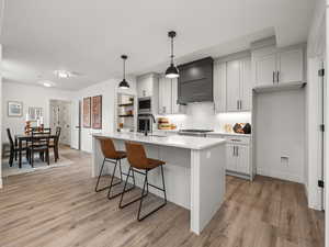 Kitchen with a center island with sink, premium range hood, light hardwood / wood-style flooring, sink, and decorative light fixtures