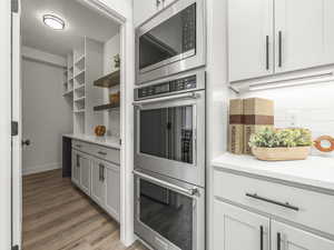 Kitchen with stainless steel appliances, light stone countertops, light wood-type flooring, white cabinetry, and a textured ceiling