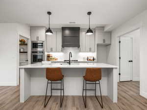 Kitchen with light wood-type flooring, stainless steel appliances, premium range hood, and an island with sink