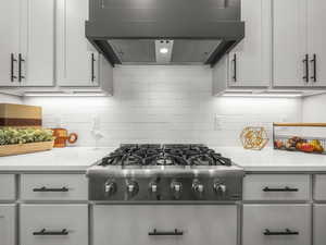 Kitchen featuring decorative backsplash, stainless steel gas cooktop, ventilation hood, white cabinetry, and light stone counters