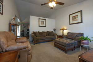 Carpeted living room with ceiling fan and vaulted ceiling