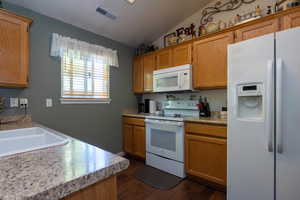 Kitchen featuring white appliances, dark wood flooring, lofted ceiling, and sink