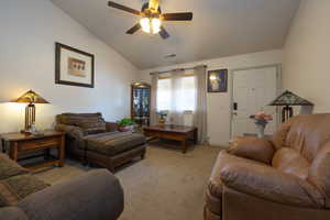 Carpeted living room featuring ceiling fan and vaulted ceiling