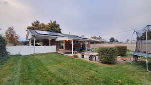 Back of property featuring solar panels, a trampoline, a patio area, and a lawn