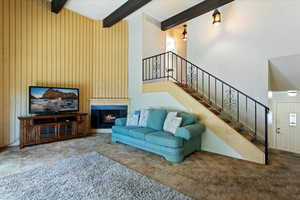 Carpeted living room featuring beamed ceiling, wood walls, a high ceiling, and a large fireplace