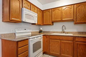 Kitchen featuring light stone counters, light tile patterned flooring, sink, and white appliances