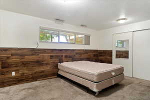 Carpeted bedroom featuring a textured ceiling, wooden walls, and a closet