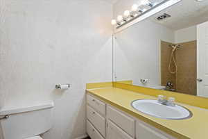 Bathroom with vanity, toilet, a textured ceiling, and tiled shower