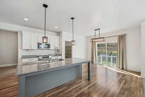 Kitchen featuring light stone countertops, wood-type flooring, sink, stainless steel appliances, and white cabinets