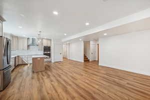 Kitchen featuring a center island, hanging light fixtures, light hardwood / wood-style floors, stainless steel appliances, and wall chimney exhaust hood