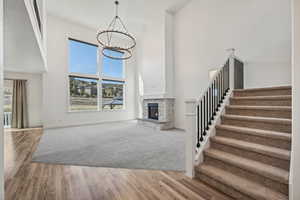 Unfurnished living room with a stone fireplace, wood-type flooring, a high ceiling, and a chandelier