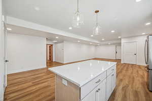 Kitchen with stainless steel fridge, a kitchen island, white cabinetry, light wood-type flooring, and decorative light fixtures