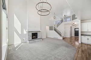 Unfurnished living room featuring a stone fireplace, hardwood / wood-style floors, a high ceiling, and ceiling fan